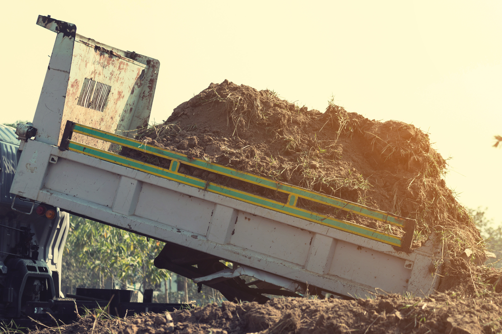 Dump truck unloading soil and preparing ground for landscaping